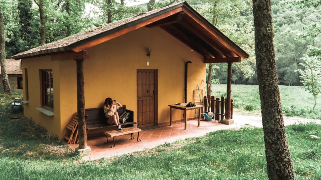 person-sitting-on-bench-in-front-of-brown-house-2410577 A woman sits on a bench outside a rustic cottage surrounded by trees and lush greenery.